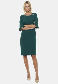 Zielona sukienka z rękawami do łokcia, ozdobiona falbankami i kokardkami. Gładki materiał, długość do kolan, minimalistyczny design, dwa dekoracyjne guziki.