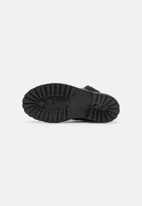Suela de bota de goma negra con surcos profundos y forma redondeada, con parte superior texturizada en negro para mayor tracción y durabilidad.