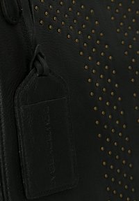 Zwarte leren tas met een gestructureerd oppervlak, gouden studs en een rechthoekig label met de opdruk "COWBOYSBAG."