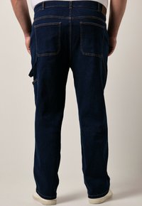 Pantalones de mezclilla azul oscuro con un diseño de pierna recta, costuras visibles, dos bolsillos traseros y un bolsillo lateral con un lazo.