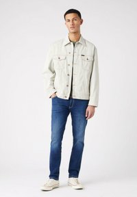 Chaqueta de mezclilla clara con cuello, dos bolsillos en el pecho y cierres de botones, combinada con jeans azules y zapatillas blancas.