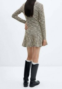Robe à manches longues en tartan avec un ourlet évasé, fabriquée en tissu texturé. Associée à des bottes noires hauteur genou et des chaussettes blanches.