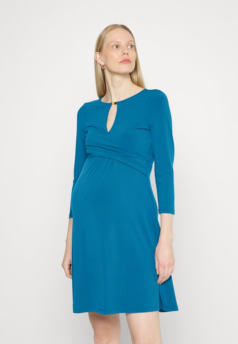 Vestido verde-água com mangas três quartos, decote em forma de chave e cintura franzida. Textura suave; comprimento até ao joelho; fendas laterais subtis.