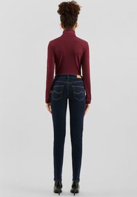 Vínový rolák s dlhými rukávmi, v kombinácii s tmavomodrými úzkymi džínami s dvoma zadnými vreckami a svetlohnedým záplatou na páse.