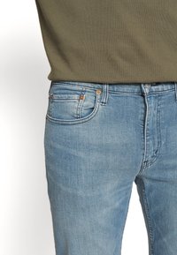 Světle modré dž�íny z denimu mají úzký střih, pět kapes a oranžové švy. Látka má hladkou texturu a mírné vyblednutí.