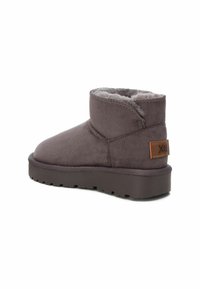 Stivale alla caviglia in suede grigio con una morbida fodera in pelliccia, punta arrotondata e suola in gomma testurizzata. Presenta una piccola patch in pelle marrone con il marchio "Xti".
