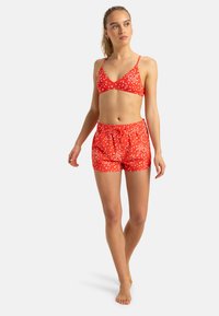 Röd badklädedsset med prickigt mönster; inkluderar en bralette-top med tunna band och shorts med elastiskt midjeband.