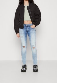 Chaqueta bomber negra, top corto verde claro, jeans skinny desgastados de color azul claro y zapatillas negras con acentos amarillos.