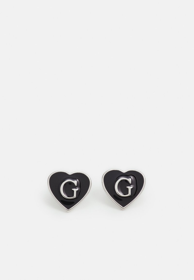 Paire de boucles d'oreilles noires en forme de cœur avec des bords argentés et une lettre G argentée en relief au centre sur fond blanc.
