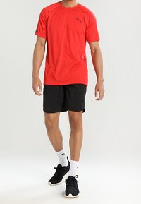 Czerwona sportowa koszulka z krótkim rękawem i czarnym logo, w zestawie z czarnymi szortami, białymi skarpetkami i czarnymi trampkami. Gładka tekstura, luźny krój.