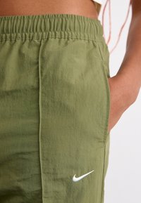 Grønne, lette shorts med elastisk talje, sidelommer og et hvidt Nike-logo broderet på venstre ben. Glat tekstur.