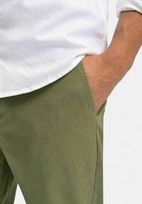 Olivgröna bomullschinos med sidoficka, rak front och en mjuk textur, kombinerat med en vit skjorta med knappar.