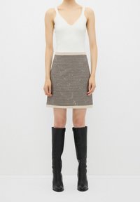 Débardeur blanc ajusté, jupe à motifs à carreaux avec des accents métalliques, et bottes noires en cuir montant jusqu'aux genoux. Texture lisse, design structuré.