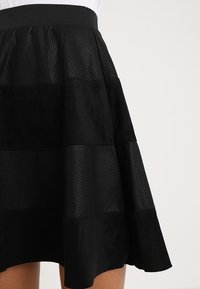 Svart kjol med en blandning av mjuk mocka och perforerat material, med en utsvängd design. Den har en åtsittande midja och ett lager-på-lager utseende.