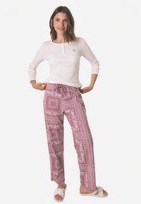 White long-sleeve top with a henley neckline, paired with pink patterned loose-fitting pants featuring bordered designs and an elastic waistband.