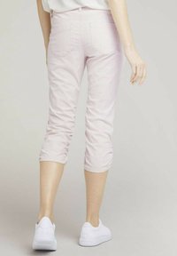 Jasnoróżowe, skrócone spodnie wykonane z miękkiego materiału, o dopasowanym kroju, z tylną kieszenią i marszczeniem na końcu. W połączeniu z białymi sneakersami.