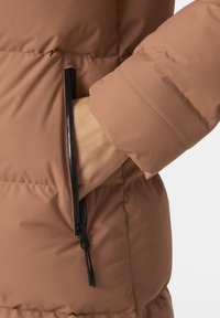Chaqueta tipo plumas en un suave tono marrón con detalles de bolsillo con cremallera. Presenta una tela lisa y texturada y un dobladillo fruncido en la cintura.