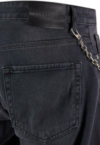 Zwarte denim jeans met een leren label, voorzien van een kettingaccessoire en een achterzak. De textuur is glad met een lichte glans.