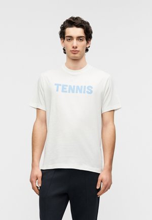 Camiseta blanca de algodón con mangas cortas, con un texto impreso en azul claro que dice "TENNIS" en el frente. Diseño simple de cuello redondo, corte relajado.