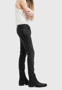 Černé džíny s slim fit střihem, klasickým designem s pěti kapsami, jemnou texturou a diskrétními švy, doplněné černými botami.