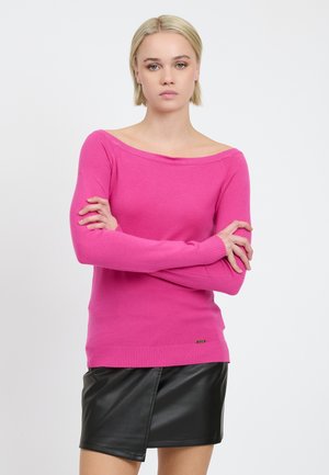 Maglione fucsia a spalle scoperte con maniche lunghe, polsini e orlo a coste, realizzato in un materiale morbido, abbinato a una mini gonna in pelle nera.