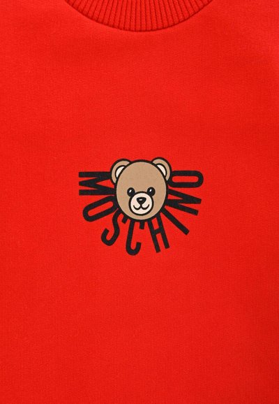 Czerwona bluza z okrągłym dekoltem z grafiką misia i napisem "MOSCHINO" w czerni, z promieniami słonecznymi wokół obrazka.