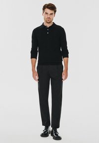 Czarna koszula polo z długim rękawem i kołnierzykiem, w połączeniu z czarnymi spodniami z plisami i błyszczącymi czarnymi butami. Prosty, monochromatyczny design.