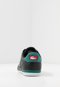 Musta nahkainen tennari, jossa on petroolinvihreät yksityiskohdat, punainen logopatch ja valkoinen pohja. Kenkässä on teksturoitu kantapää ja virtaviivainen, pyöreä muotoilu.