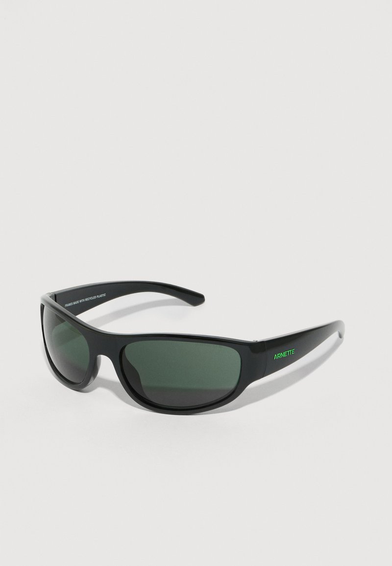 Černé sluneční brýle s plastovým rámečkem a zelenými skly. Elegantní, zakřivený design s nápisem značky "ARNETTE" zelenou barvou na straně.