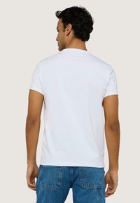 Camiseta blanca de algodón con cuello redondo clásico, mangas cortas y un diseño de espalda sin costuras. Combinada con vaqueros de mezclilla azules.