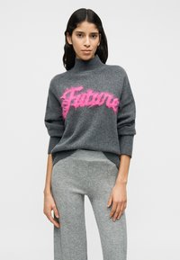 Γκρι πλεκτό πουλόβερ με ψηλό λαιμό και χαλαρή εφαρμογή, με αφράτο ροζ κείμενο «Future». Συνδυάζεται με γκρι υφασμάτινο παντελόνι.