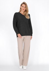 Luźny ciemnoszary sweter dzianinowy z dekoltem w serek, w zestawieniu z beżowymi spodniami szerokimi oraz białymi sneakersami. Miękka tekstura, casualowy design.