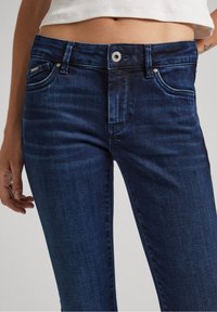 Dark blue denim jeans with a slim fit, featuring five pockets, subtle fading, and a standard button closure at the waistband.