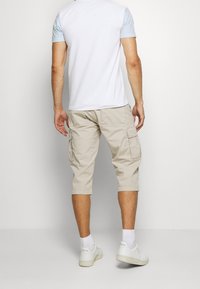 Bermudas beige de corte hasta la rodilla, con bolsillos de parche y dobladillos enrollados. Llevadas con una camiseta blanca y azul claro y zapatillas blancas.