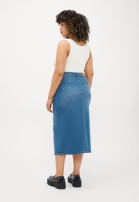Denim krilo ima srednjo dolžino, prilegajoč pas, dve zadnji žepki in svetlo modro pranje. Kombinirano z belim topom s tankimi naramnicami in črnimi čevlji.