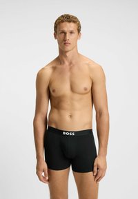 Schwarze Boxershorts mit einem weißen, mit Logo bedruckten Bund. Hergestellt aus glattem Stoff, mit enger Passform und klassischem Design.