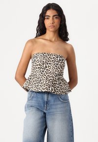 Top brez naramnic z leopardjim vzorcem in peplum robom, narejen iz lahkega materiala, v kombinaciji z visokimi svetlo modrimi kavbojkami.