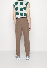 Mouwloos topje met groene stippen op een lichte achtergrond, gecombineerd met een paarse broek en grijze sneakers. Eenvoudig ontwerp, comfortabele pasvorm.