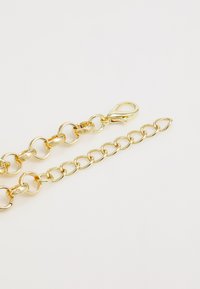 Chaîne en métal doré, composée de maillons ovales et ronds, avec un fermoir à une extrémité et une surface lisse et brillante.