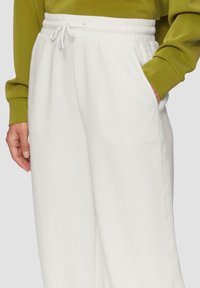 Białe dresy z elastycznym pasem w talii, bocznymi kieszeniami oraz nadrukowanym logo na nogawce. Miękka tkanina z luźnym krojem.