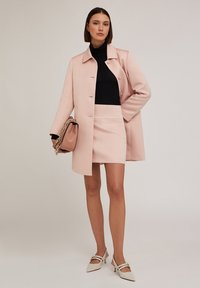 Ljust rosa skräddarsydd kappa med krage, tillsammans med en svart polotröja och matchande minikjol. Vita klackskor och en brun handväska.