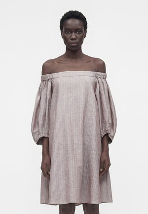 Γυναίκα με φαρδιά, ανοιχτό ροζ φόρεμα εκτός ώμων με κάθετες λευκές ρίγες και φουσκωτά μανίκια τριών τετάρτων.