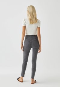 Jeans skinny taille haute gris foncé avec poches arrière, associés à un haut blanc à manches courtes. Coupe slim et texture lisse.
