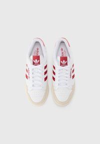 Zapatillas Adidas en blanco con rayas rojas, con puntera perforada, cuello acolchado y suela de goma. Diseño clásico con cordones.