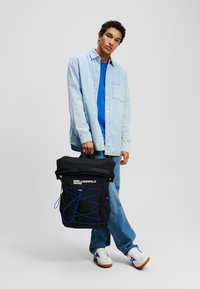 Fekete hátizsák kék gumihúzóval, tetején fogantyúval és elülső zsebbel, „Karl Lagerfeld Jeans” logóval fehér színben.