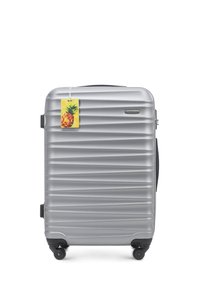 Silver hard-shell suitcase with ribbed design, black wheels, and a yellow pineapple tag. Features a smooth texture and sturdy handles.