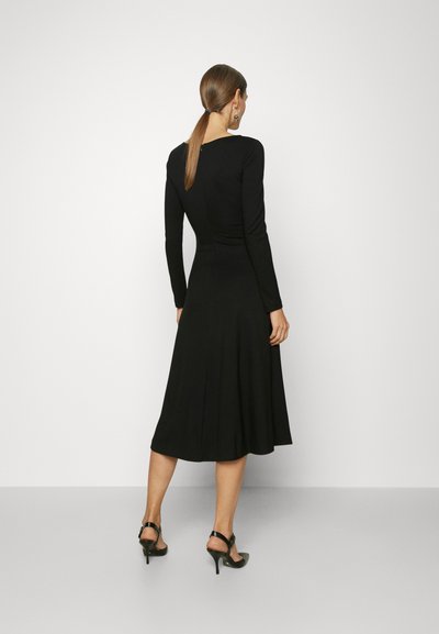 Μαύρο φόρεμα με μακριά μανίκια, εφαρμοστό κορσέ και φαρδύ φούστα, κατασκευασμένο από λείο ύφασμα. Διαθέτει διακριτική λεπτομέρεια με άνοιγμα στην πλάτη και μήκος έως το γόνατο.