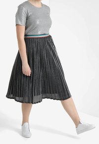 Gray metallic short-sleeve shirt, paired with a pleated black skirt featuring a multi-colored waistband, worn with white sneakers.