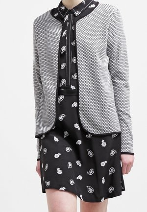 Outfit in bianco e nero composto da un vestito a fantasia con design paisley e un giubbotto strutturato con motivo a nido d'ape, scollatura tonda.