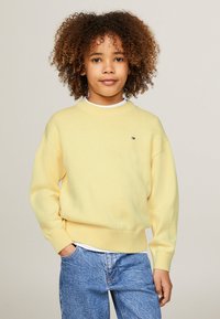 Maglione giallo realizzato in un morbido tessuto, con polsini e orlo a coste, abbinato a jeans azzurri chiari. Piccolo logo sul lato sinistro anteriore.